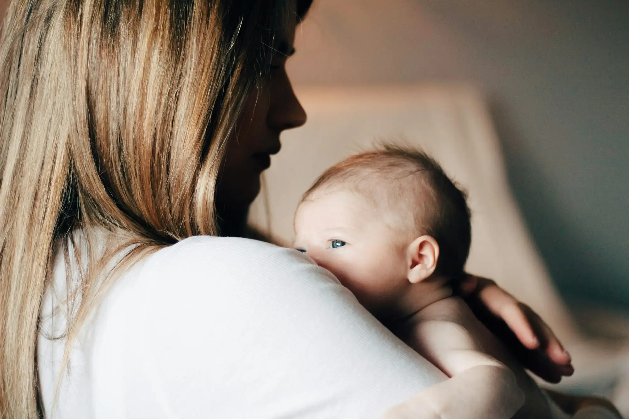 Mor i hvid t-shirt holder sin baby tæt ind til skulderen