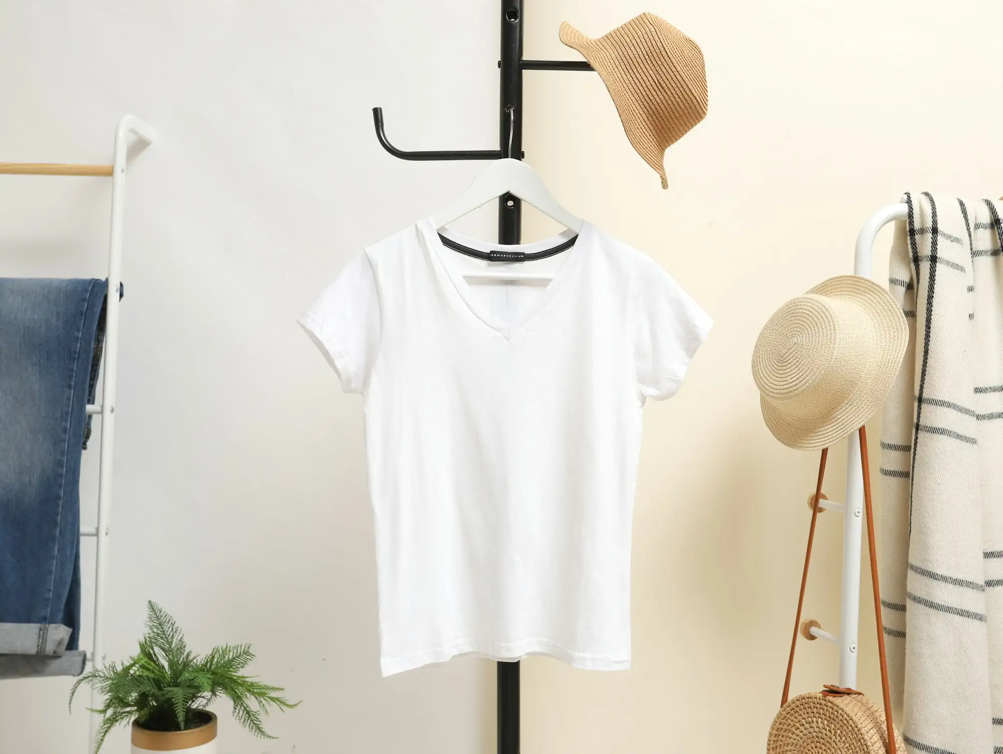 Hvid T-shirt på en bøjle ved et tøjstativ med hatte og en plante