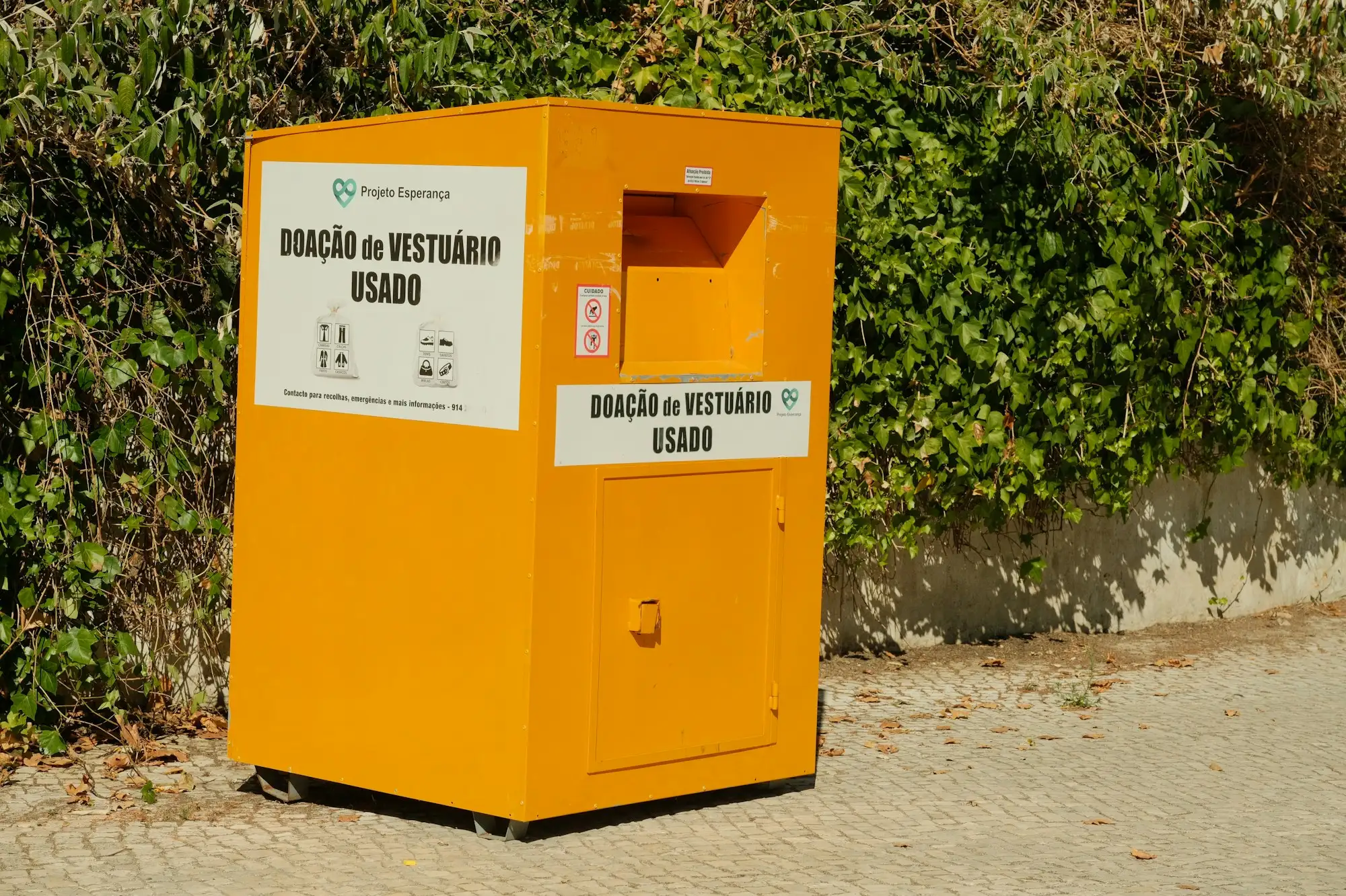 Gul indsamlingscontainer til brugt tøj foran en mur med efeu