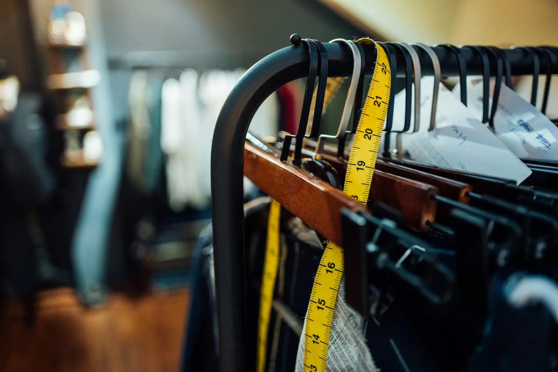 Gult målebånd hænger over en tøjstang med bøjler i en butik